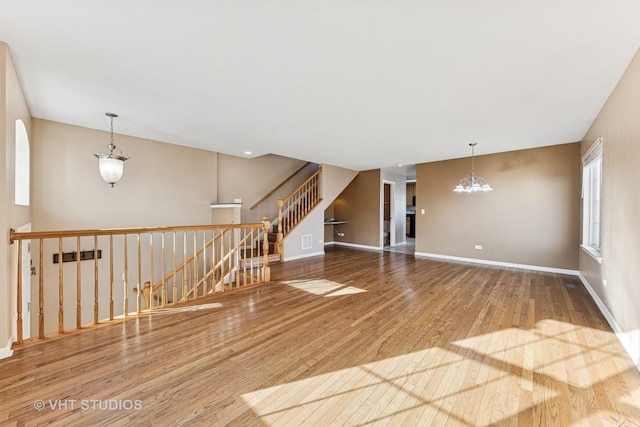 unfurnished room featuring stairway, a notable chandelier, wood finished floors, and baseboards