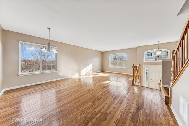 unfurnished living room featuring a chandelier, visible vents, stairway, and hardwood / wood-style flooring