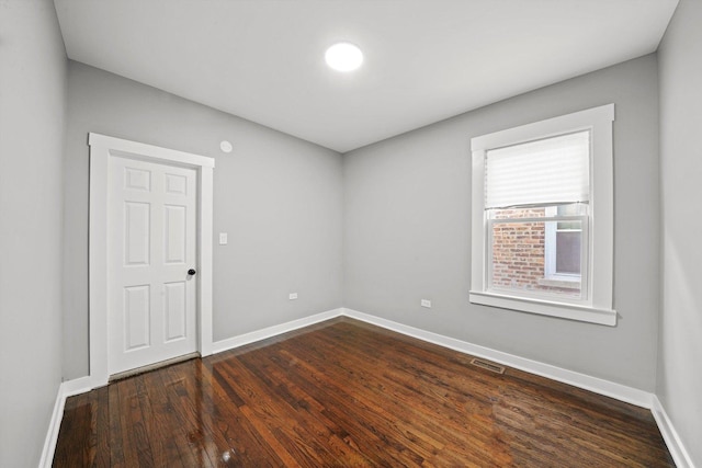 unfurnished room with baseboards, visible vents, and dark wood-type flooring