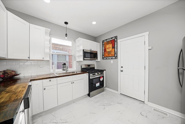 kitchen featuring butcher block counters, appliances with stainless steel finishes, white cabinetry, open shelves, and a sink