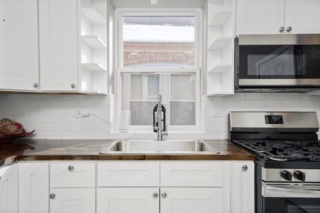 kitchen with open shelves, stainless steel appliances, dark countertops, white cabinetry, and a sink