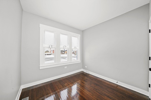 empty room with dark wood-style floors, visible vents, and baseboards