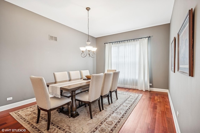 dining space with an inviting chandelier, baseboards, visible vents, and wood finished floors