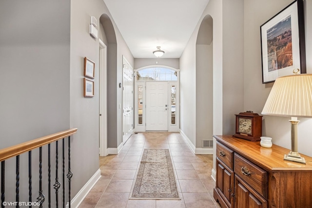 foyer entrance featuring visible vents, arched walkways, baseboards, and light tile patterned flooring