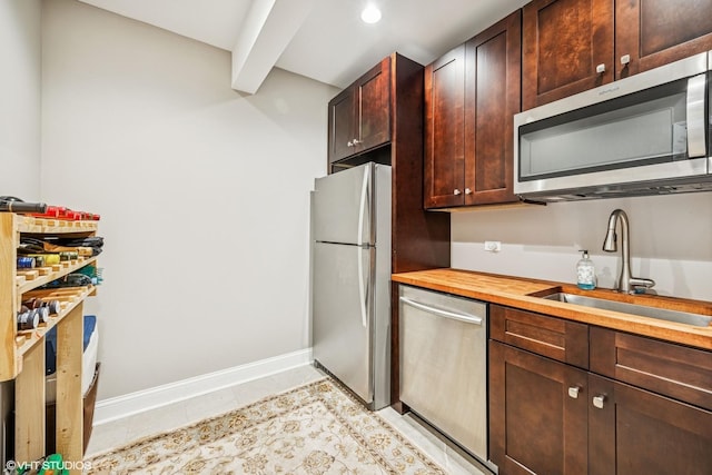 kitchen with stainless steel appliances, wooden counters, light tile patterned flooring, a sink, and baseboards