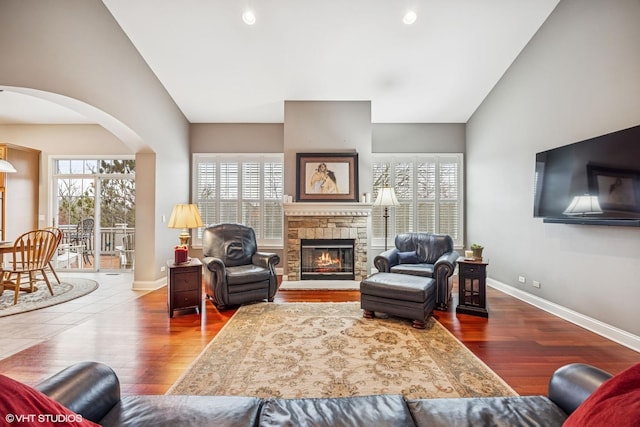 living room featuring vaulted ceiling, a stone fireplace, baseboards, and wood finished floors