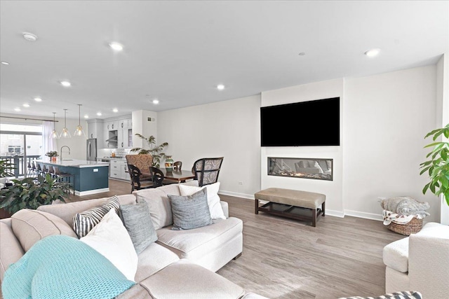 living room featuring baseboards, a glass covered fireplace, wood finished floors, and recessed lighting