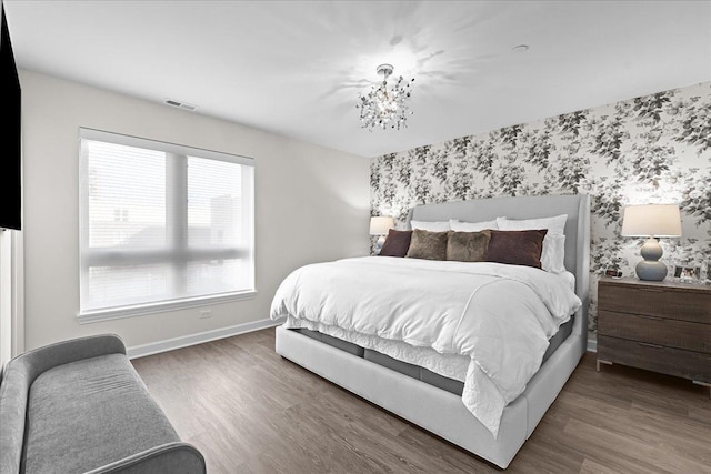 bedroom with an accent wall, wood finished floors, visible vents, baseboards, and wallpapered walls