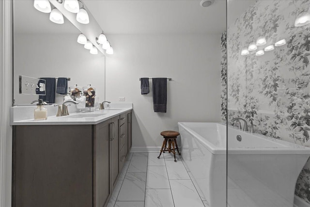 full bath featuring double vanity, marble finish floor, a freestanding tub, and a sink