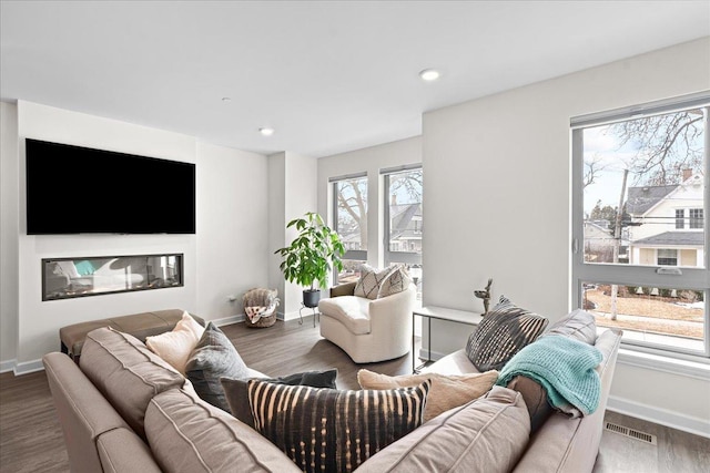 living area featuring a glass covered fireplace, wood finished floors, visible vents, and baseboards