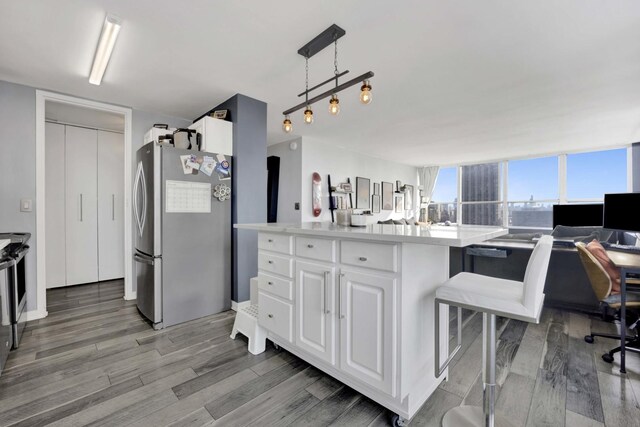 kitchen featuring pendant lighting, light countertops, freestanding refrigerator, white cabinets, and wood finished floors