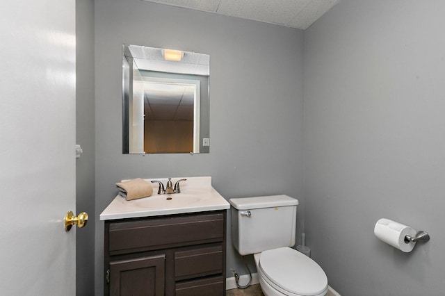 half bath featuring a paneled ceiling, baseboards, vanity, and toilet