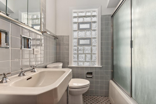 full bathroom with toilet, a sink, a wealth of natural light, and tile walls