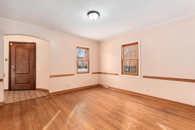 empty room with baseboards, visible vents, arched walkways, ornamental molding, and wood finished floors