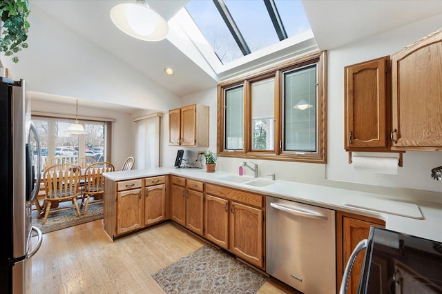 kitchen featuring vaulted ceiling with skylight, appliances with stainless steel finishes, a peninsula, light wood-style floors, and a sink