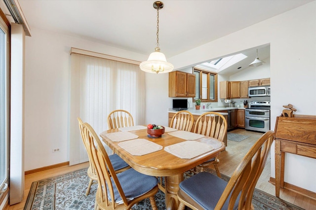 dining space featuring vaulted ceiling with skylight, light wood-style flooring, and baseboards