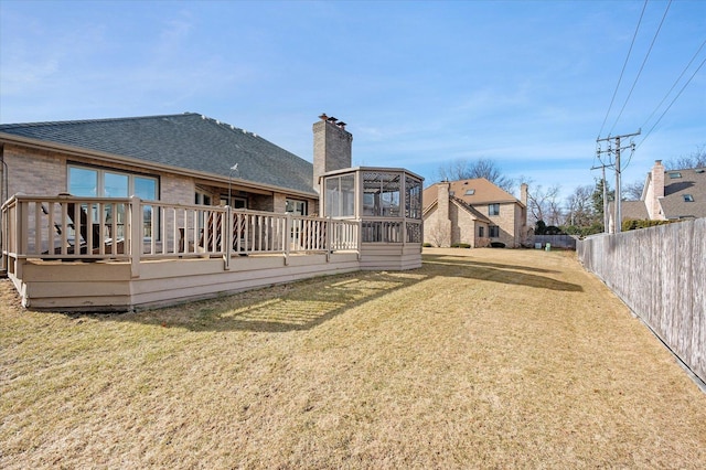 rear view of property featuring a lawn, a chimney, fence, a deck, and brick siding