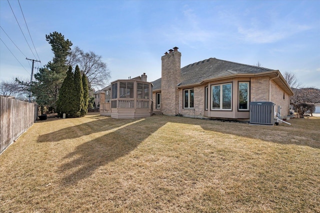 back of property with central AC unit, a lawn, a sunroom, a chimney, and fence