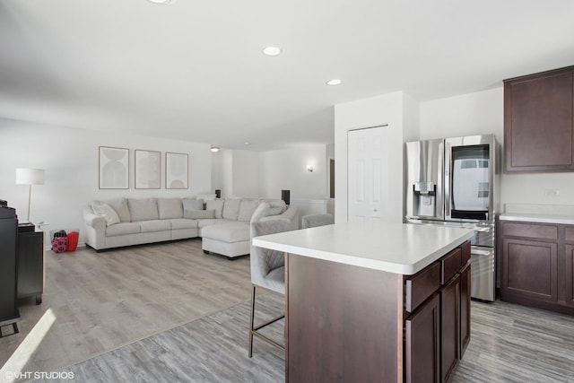 kitchen with a kitchen island, light wood-style floors, open floor plan, light countertops, and stainless steel fridge