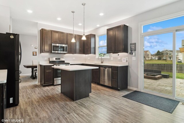 kitchen with stainless steel appliances, a sink, a kitchen island, hanging light fixtures, and light countertops