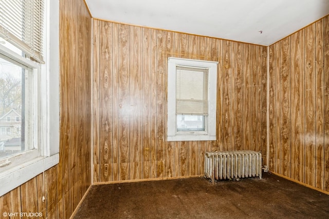 carpeted spare room with wood walls and radiator heating unit