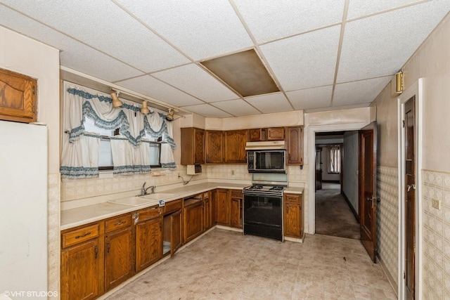 kitchen with black microwave, a sink, light countertops, brown cabinetry, and gas range oven