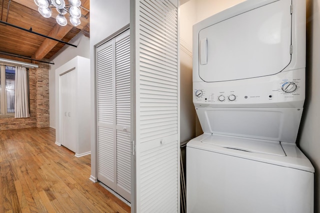 clothes washing area featuring laundry area, light wood finished floors, wood ceiling, brick wall, and stacked washing maching and dryer