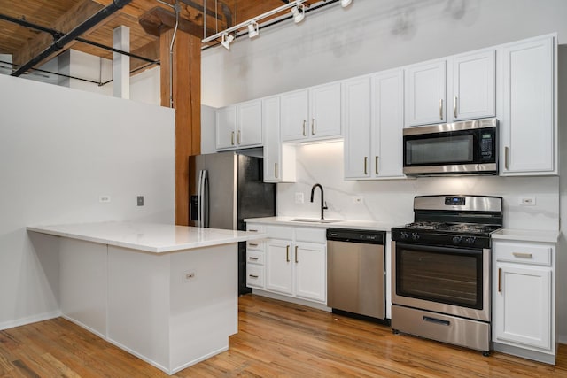 kitchen featuring appliances with stainless steel finishes, a peninsula, light countertops, white cabinetry, and a sink