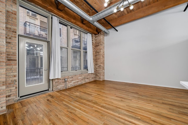 unfurnished room featuring beam ceiling, light wood-style flooring, wood ceiling, track lighting, and brick wall