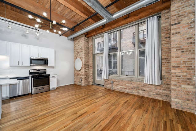 kitchen featuring brick wall, appliances with stainless steel finishes, light countertops, white cabinetry, and pendant lighting