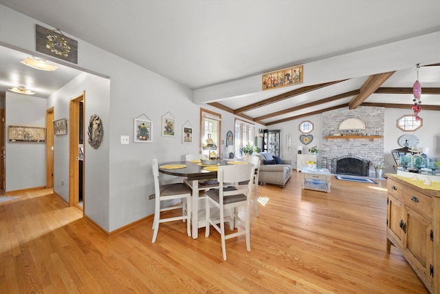 dining room featuring lofted ceiling with beams, light wood-type flooring, baseboards, and a fireplace