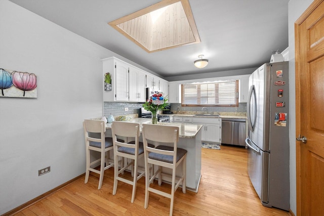 kitchen featuring light wood-type flooring, appliances with stainless steel finishes, a peninsula, white cabinets, and a sink