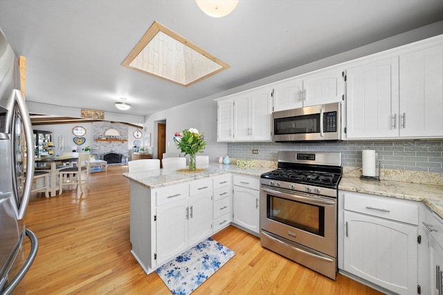 kitchen featuring light wood-style flooring, a large fireplace, appliances with stainless steel finishes, a peninsula, and white cabinets