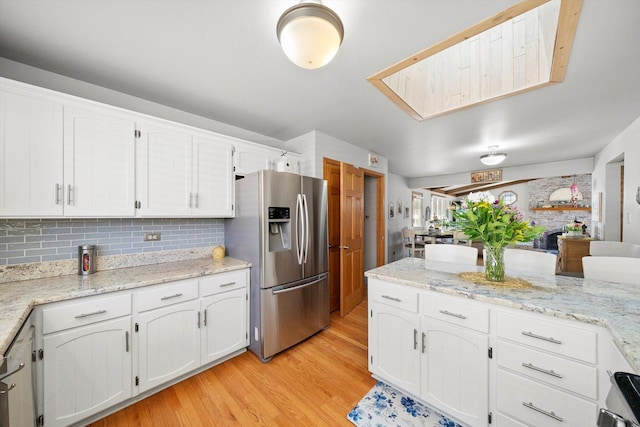 kitchen with light stone countertops, light wood-style flooring, white cabinets, stainless steel refrigerator with ice dispenser, and backsplash