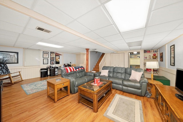 living room featuring visible vents, light wood-style flooring, a drop ceiling, stairway, and wainscoting