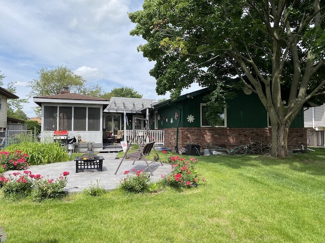 rear view of property featuring a patio, a sunroom, a chimney, a lawn, and brick siding