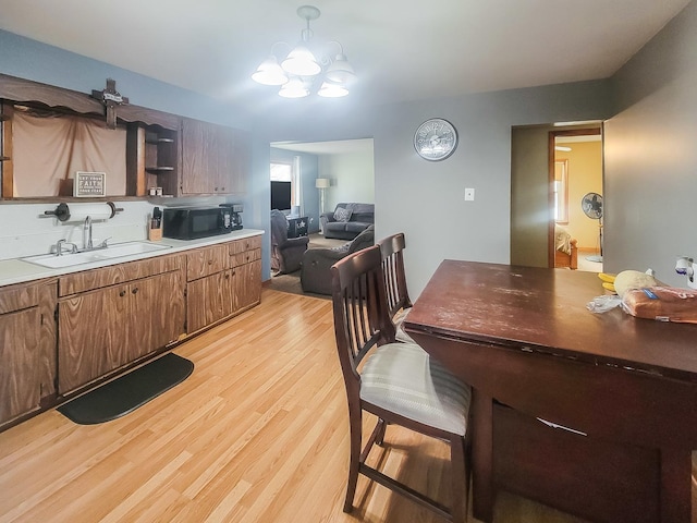 kitchen with light wood-style flooring, a sink, black microwave, open shelves, and a notable chandelier