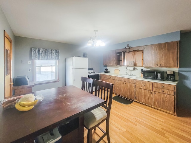 kitchen with white appliances, an inviting chandelier, light countertops, light wood-style floors, and a sink