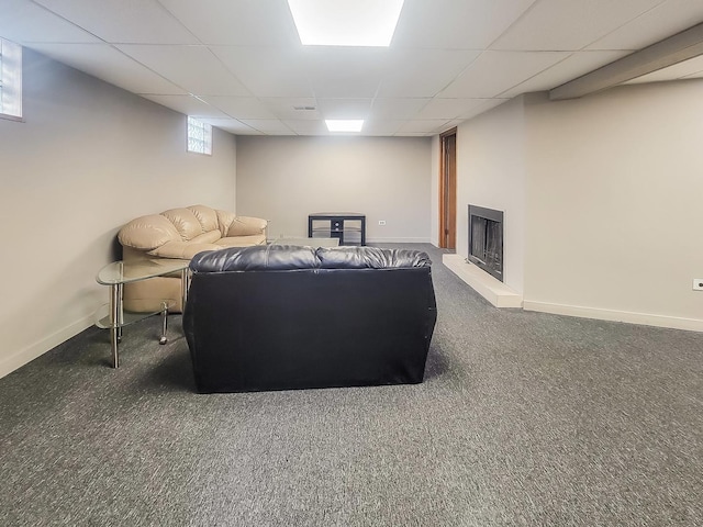 living area with a paneled ceiling, baseboards, a fireplace with raised hearth, and carpet flooring