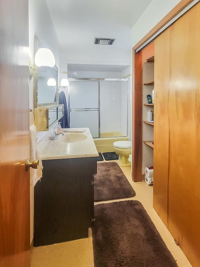 full bath featuring visible vents, vanity, toilet, and bath / shower combo with glass door