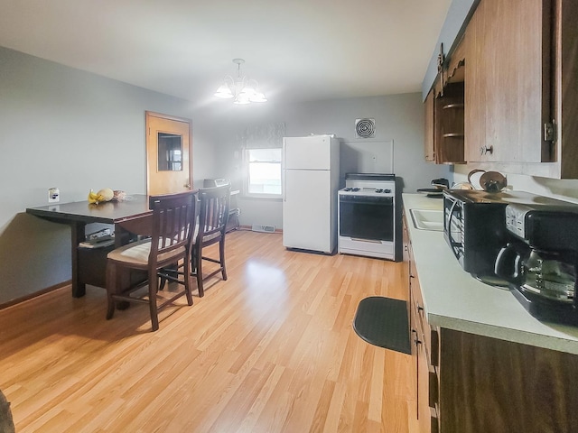 kitchen with decorative light fixtures, a notable chandelier, light countertops, light wood-type flooring, and white appliances