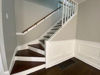 stairway with wainscoting, a decorative wall, and wood finished floors