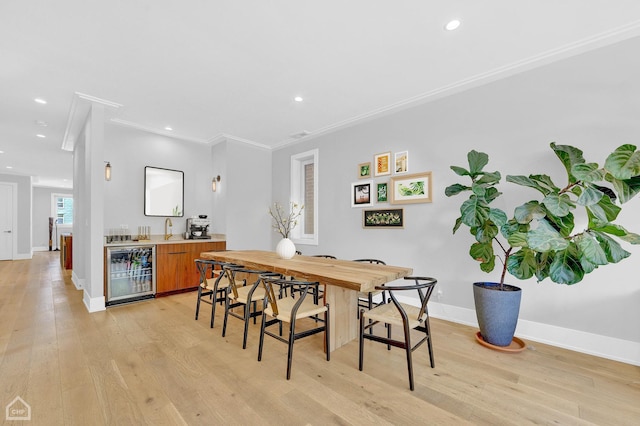 dining area with a dry bar, baseboards, wine cooler, crown molding, and light wood-type flooring