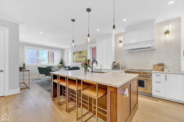 kitchen featuring light stone counters, pendant lighting, high end stainless steel range oven, white cabinets, and an island with sink