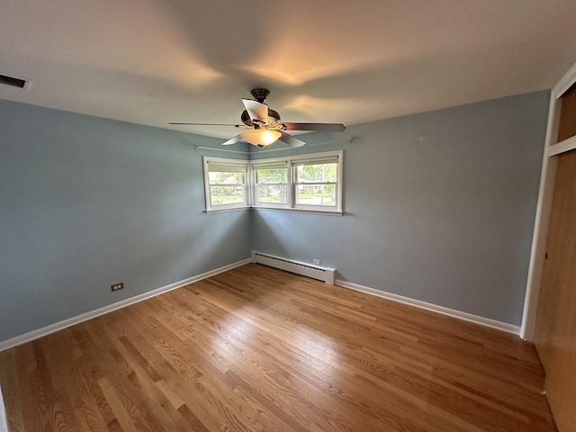 empty room featuring a baseboard heating unit, wood finished floors, a ceiling fan, and baseboards