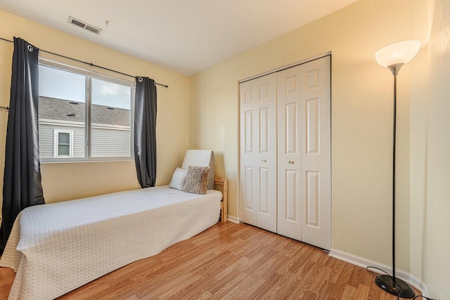 bedroom with a closet, visible vents, light wood-style flooring, and baseboards