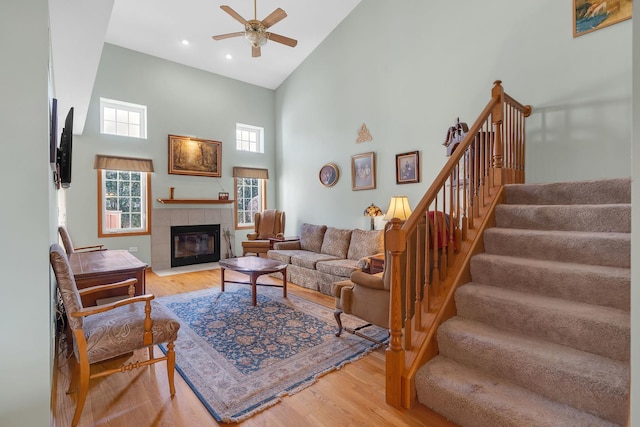 living room featuring a ceiling fan, a high ceiling, a fireplace, stairs, and light wood-type flooring