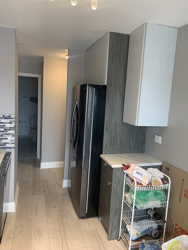 kitchen with light wood-type flooring, baseboards, light countertops, and freestanding refrigerator