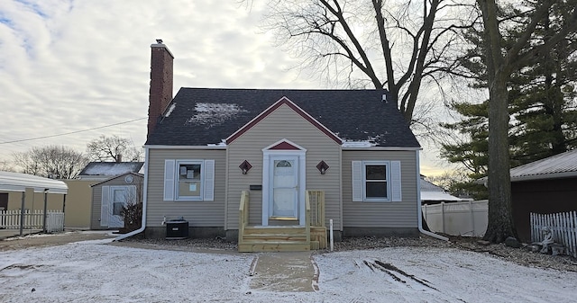 bungalow-style home with entry steps, a shingled roof, a chimney, and fence