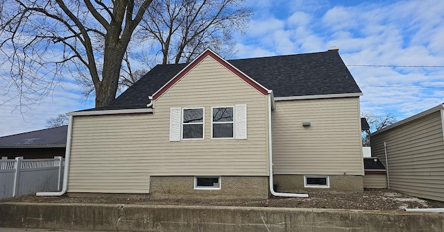 view of side of property featuring roof with shingles and fence